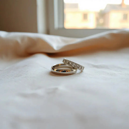 Two wedding bands on neutral fabric under soft natural light, showing metal texture and gentle sparkle