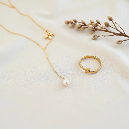 Gold necklace, earrings, bracelet and ring arranged on neutral fabric with soft lighting