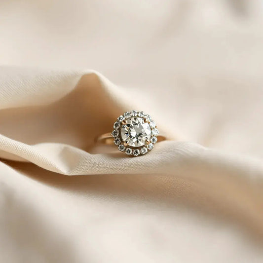 Diamond halo engagement ring with central stone and surrounding halo on a neutral fabric background