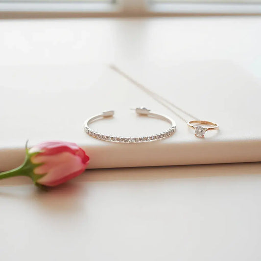 Assorted diamond jewelry including studs, a ring, and a bracelet arranged on a light neutral background