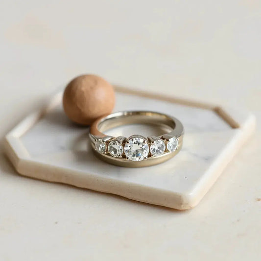 Three-stone trilogy rings with a polished metal band on a light neutral background