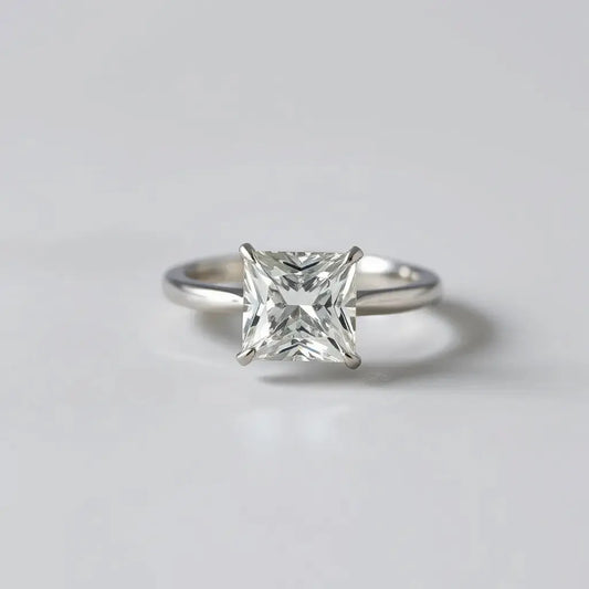 Princess cut diamond ring with square facets and a simple band on a light gray background