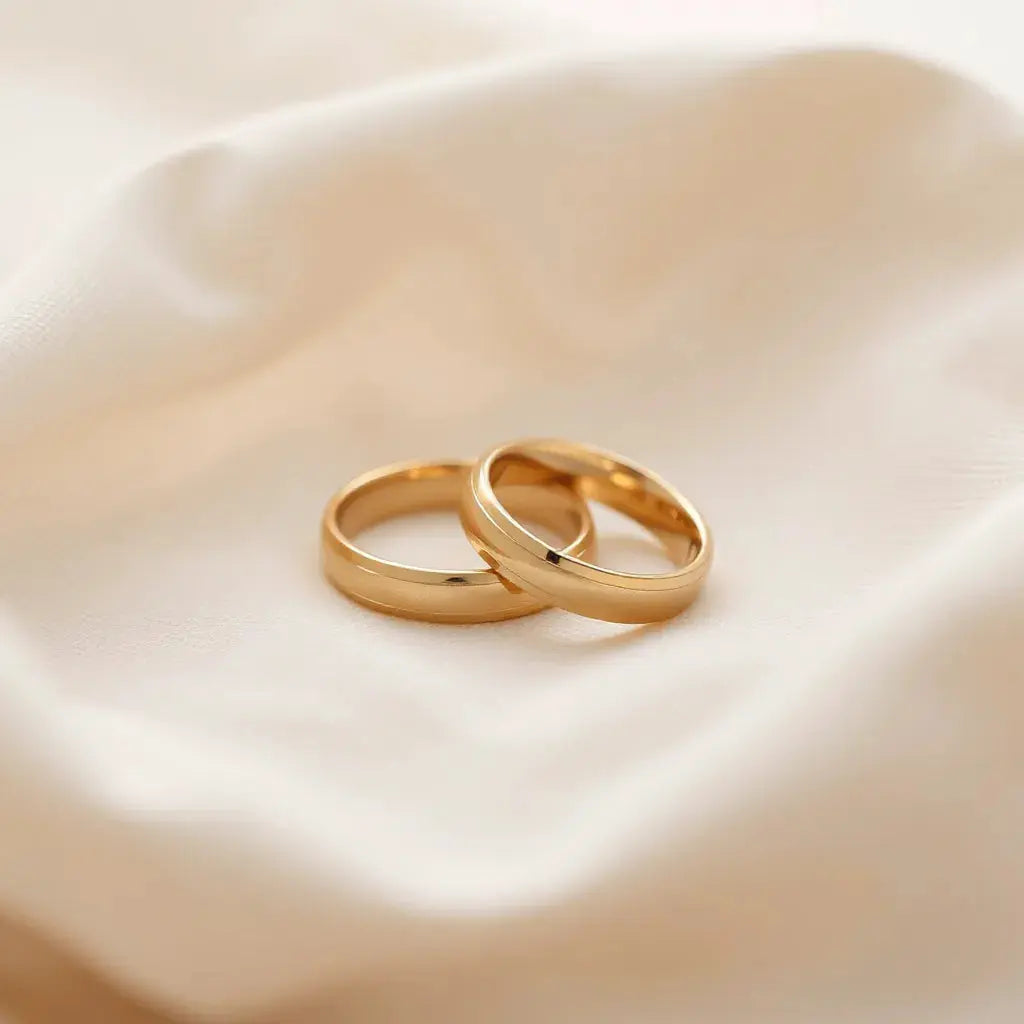 Two smooth gold comfort-fit wedding bands on neutral fabric with softly lit inner contours