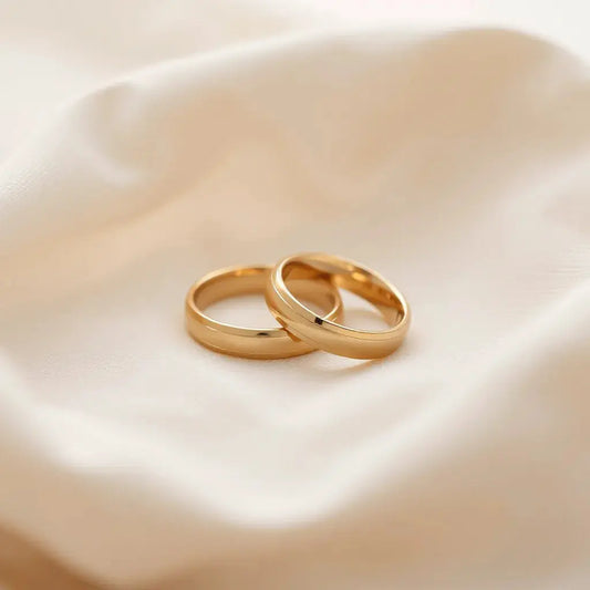 Two smooth gold comfort-fit wedding bands on neutral fabric with softly lit inner contours