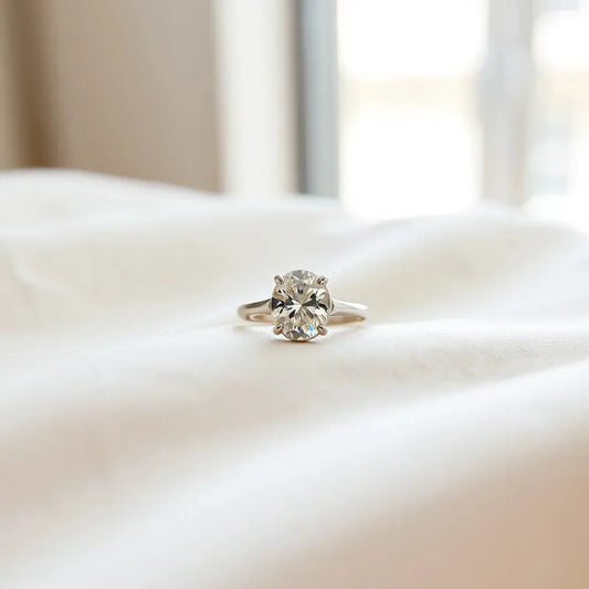 Oval diamond ring on neutral fabric with window light highlighting the oval sparkle and band details