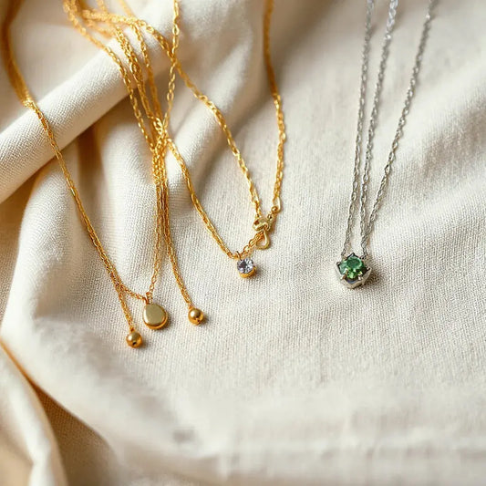 Layered gold and silver necklaces with a small pendant arranged on neutral fabric