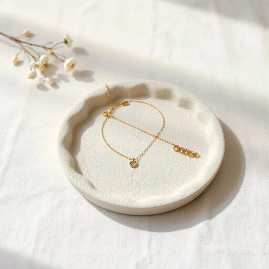 Minimal gold pendant, bracelet, and small stud earrings on a calm neutral linen tray