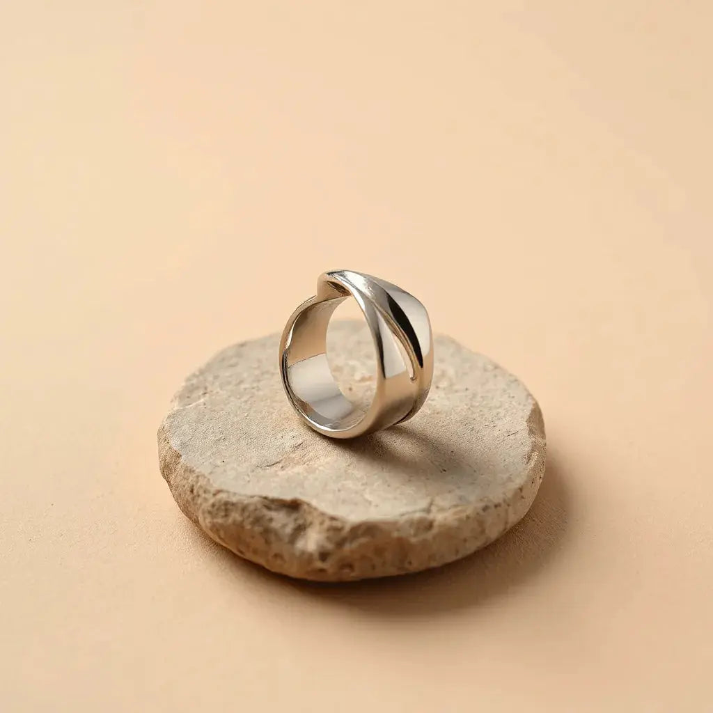 Modern sculptural ring with sculpted metal form and polished highlights on a neutral stone surface