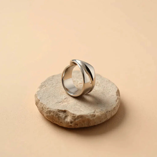 Modern sculptural ring with sculpted metal form and polished highlights on a neutral stone surface
