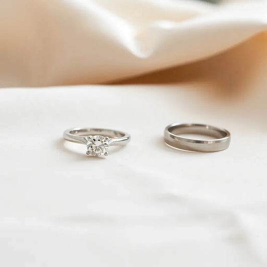 Two engagement rings with a diamond solitaire and sleek band on a neutral fabric background