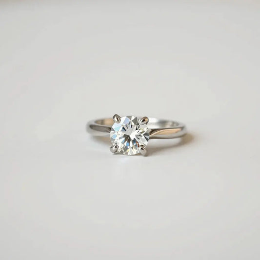 Four-prong solitaire diamond ring with prongs holding the center stone in soft studio light