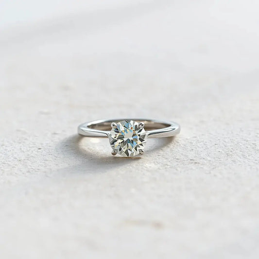 A solitaire diamond ring with a single round brilliant stone in a minimalist prong setting on a neutral background
