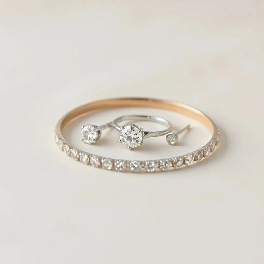Minimal lab grown diamond ring, bracelet, and stud earrings arranged on a neutral satin surface