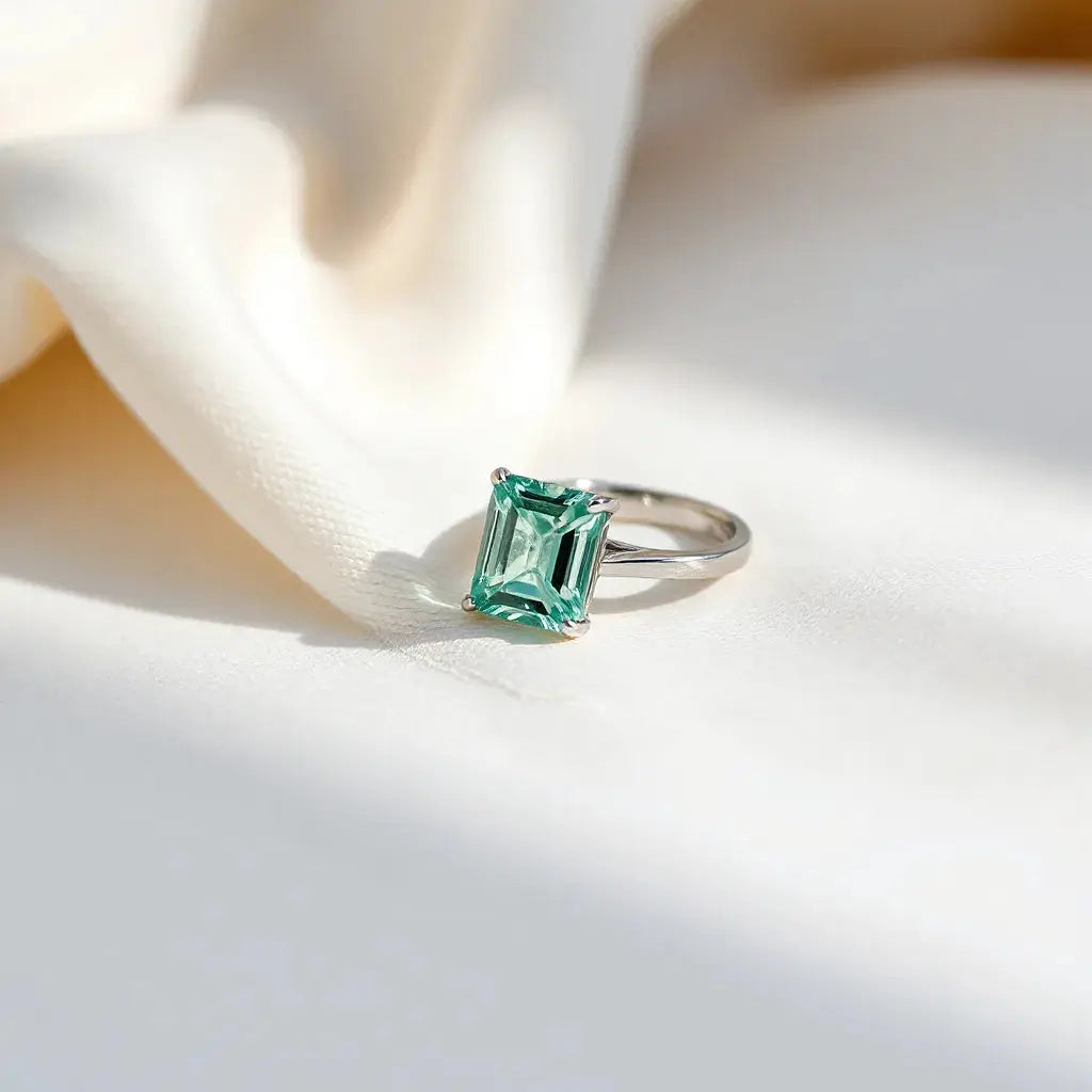 Emerald-cut diamond ring with a minimalist band on neutral fabric under soft daylight