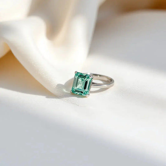Emerald-cut diamond ring with a minimalist band on neutral fabric under soft daylight