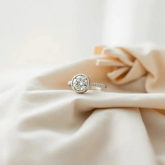 Bezel-set engagement ring with a diamond center resting on neutral fabric under soft natural light
