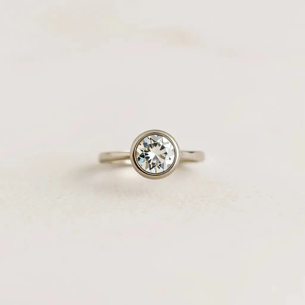 Bezel-set diamond engagement ring with a sleek metal setting on a neutral background