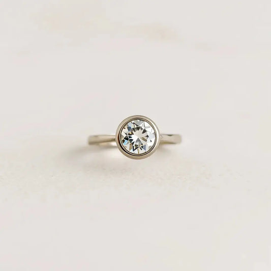 Bezel-set diamond engagement ring with a sleek metal setting on a neutral background