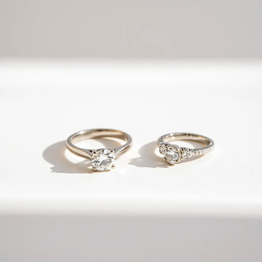 Two engagement rings with diamond center stones displayed on a light neutral background