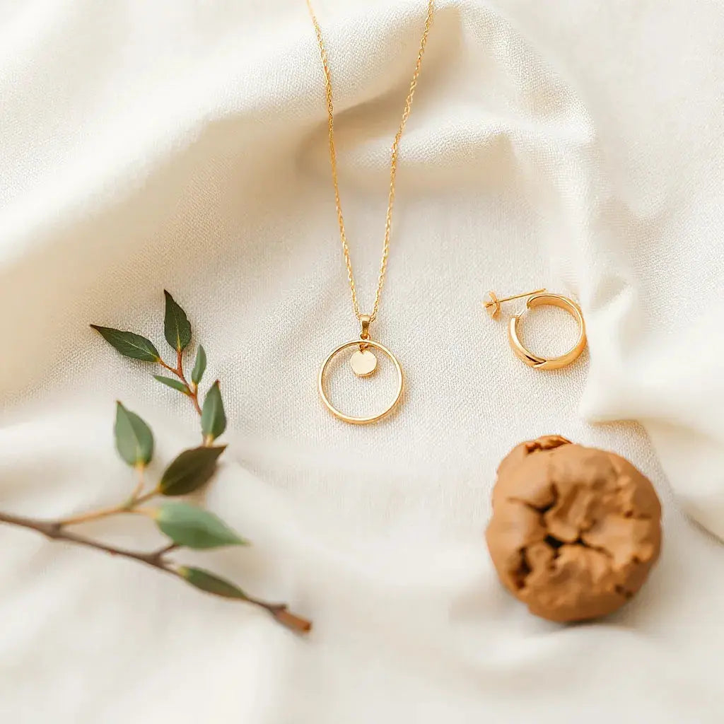 Delicate gold necklace, hoops, slim bracelet, and ring arranged on neutral fabric with soft natural light