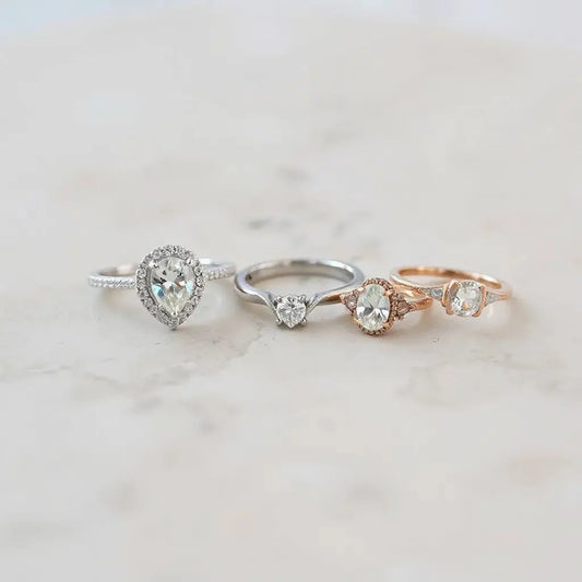 Three distinct engagement rings with different center cuts and elegant settings on a light stone surface