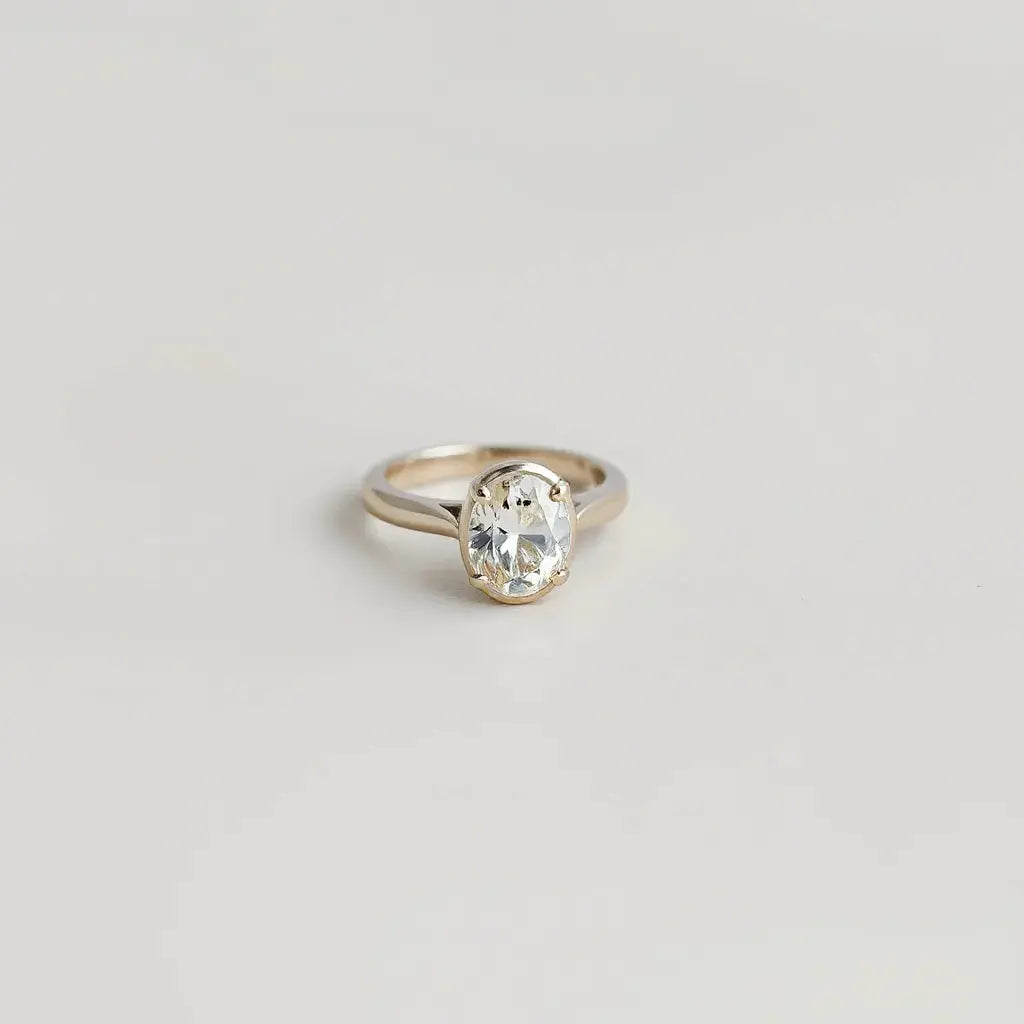 Oval diamond ring with a centered oval gemstone and detailed metal band on a neutral background