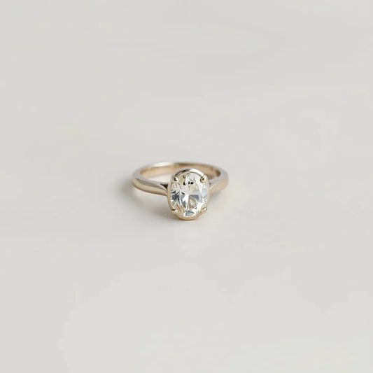 Oval diamond ring with a centered oval gemstone and detailed metal band on a neutral background
