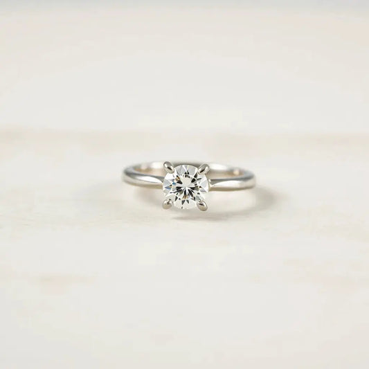 Four-prong solitaire diamond ring with prongs and centered stone on a clean light background