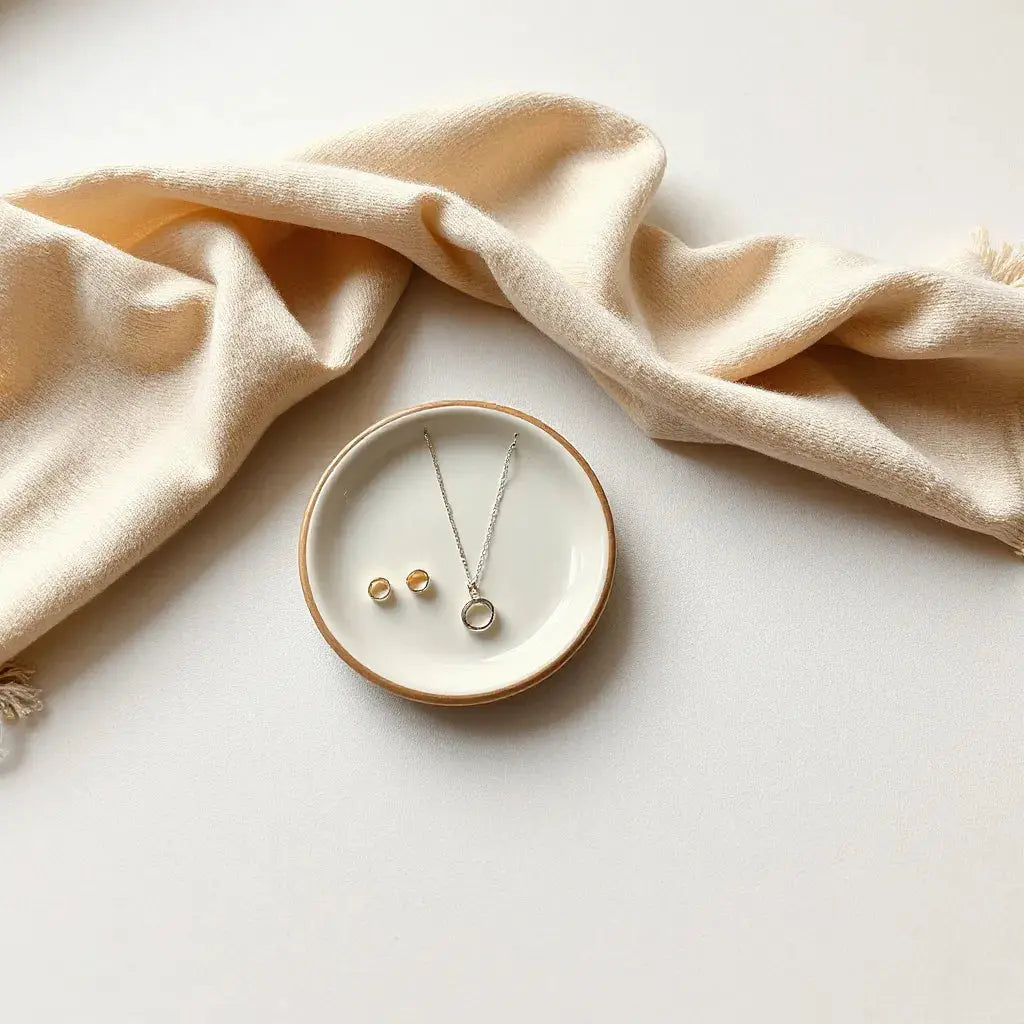 Delicate silver and gold jewelry set styled with a cream scarf and ceramic dish in warm light