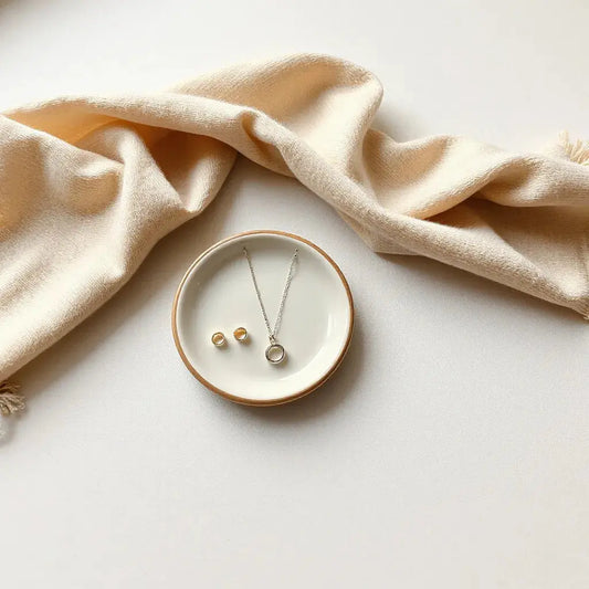 Delicate silver and gold jewelry set styled with a cream scarf and ceramic dish in warm light