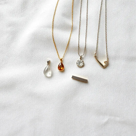 Assorted elegant pendants on a light fabric with delicate chains in soft natural light