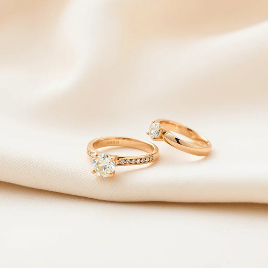 Two 18k gold engagement rings on neutral fabric, one showing a diamond solitaire setting and detailed prongs