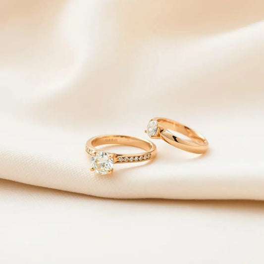 Two 18k gold engagement rings on neutral fabric, one showing a diamond solitaire setting and detailed prongs